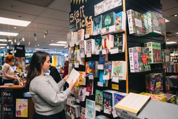 A person reads a book inside Unity books, while standing in front of a colourful bookshelf.