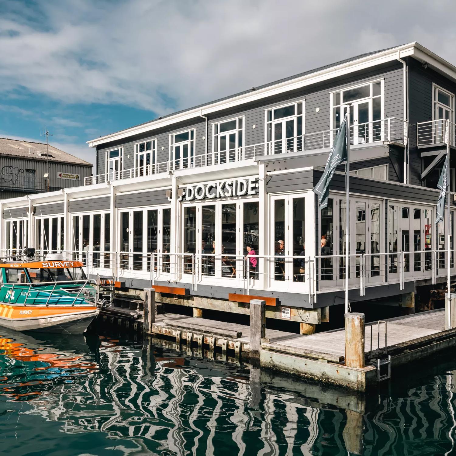 The exterior of Dockside, floating on the water off Queens Wharf, with a boat parked up beside.