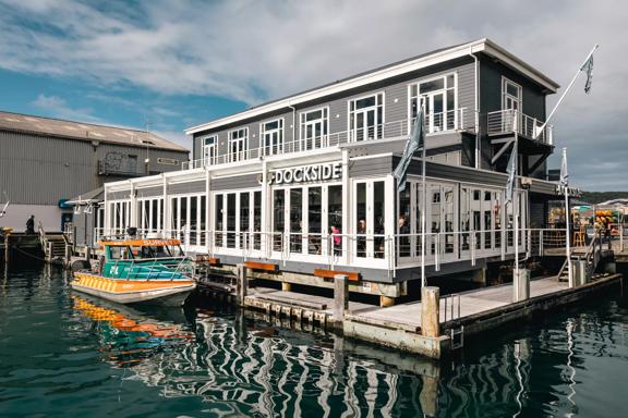 The exterior of Dockside, floating on the water off Queens Wharf, with a boat parked up beside.