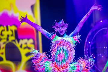 A model poses with raised arms, wearing a dress and sunglasses made of glowsticks.