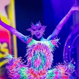 A model poses with raised arms, wearing a dress and sunglasses made of glowsticks.