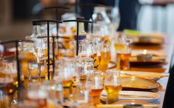 Many glasses of beer sit on a table surrounded by plates, chopsticks, and bowls.