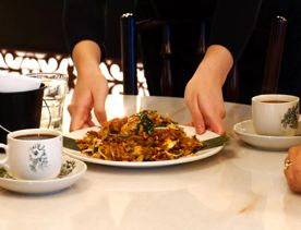 A plate of noodles is placed on a table between two coffees at Little Penang.