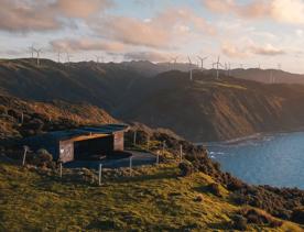 A small structure on a cliffside in the Mākara Walkway in the Wellington Region with the West Wind Farm visible in the background.