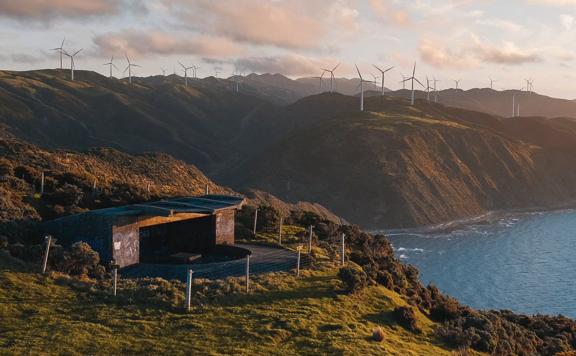 A small structure on a cliffside in the Mākara Walkway in the Wellington Region with the West Wind Farm visible in the background. 
