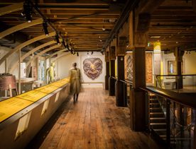 A person walking in a gallery space in the Wellington Museum with wood floors and ceilings.