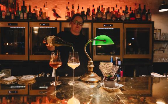 A bartender stands behind the bar pouring two glasses of wine at Puffin, a chic winebar in Te Aro, Wellington.