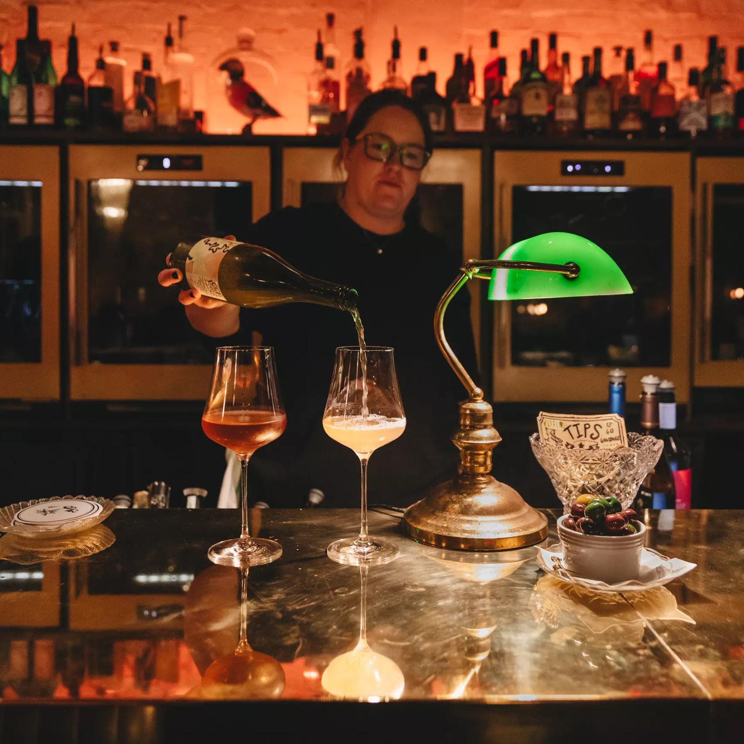 A bartender stands behind the bar pouring two glasses of wine at Puffin, a chic winebar in Te Aro, Wellington.
