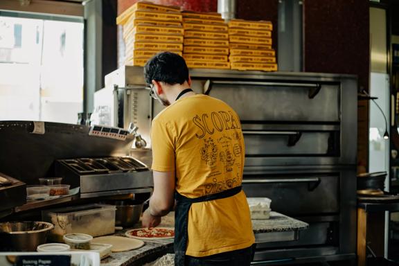 A chef from Scopa making pizzas with their back turned, wearing a yellow Scopa shirt.