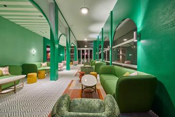 A modern lounge space with multiple seating areas, geometric patterned tiles, green walls and archways.