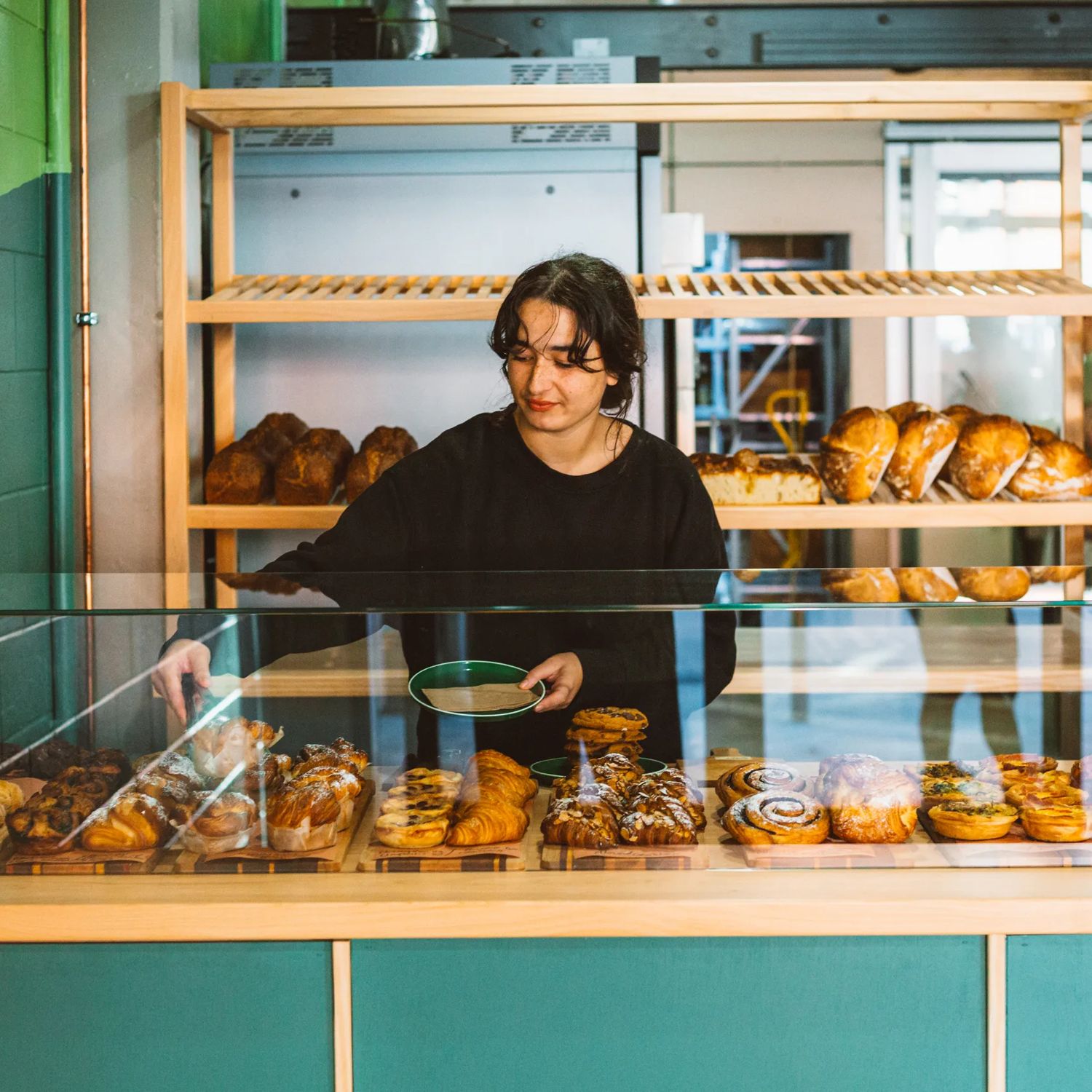 A baker uses tongs to pick up a pastry from the glass cabinet and put it on a plate.