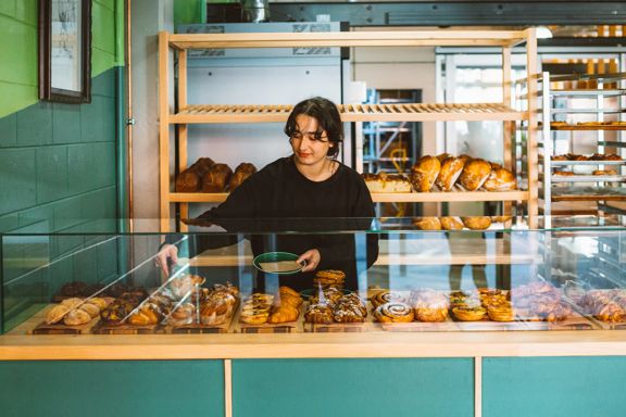 A baker uses tongs to pick up a pastry from the glass cabinet and put it on a plate.