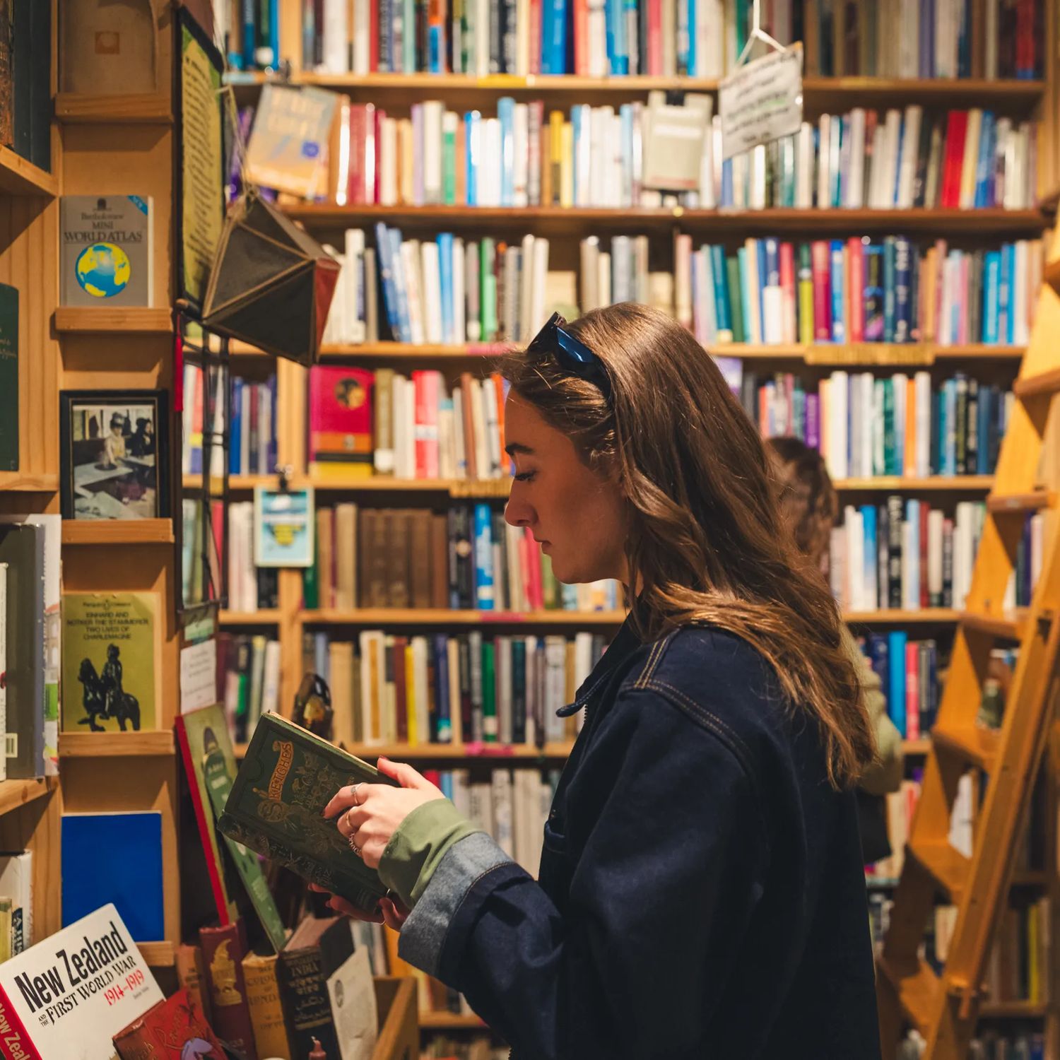 A person reads a book inside Pegasus Books, while standing in front of a colourful bookshelf.