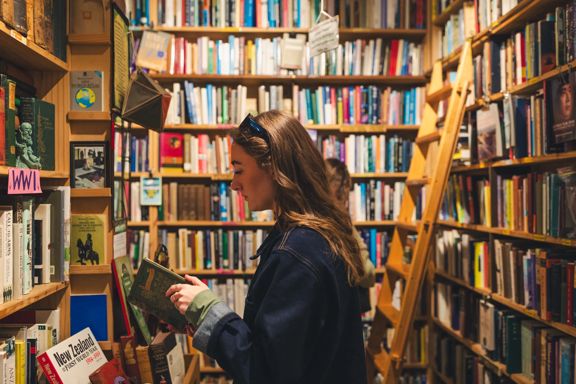 A person reads a book inside Pegasus Books, while standing in front of a colourful bookshelf.