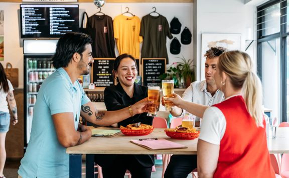 Four friends raising their beer glasses at Heyday Beer co while enjoying fries.