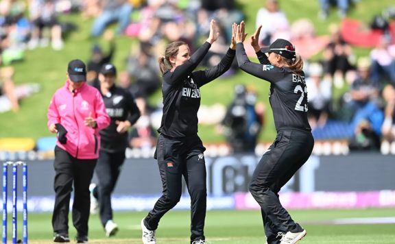 2 Cricket players high fiving on the field.