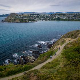 A birdseye view of three cyclists riding along Te Onepoto Loop Track in Whitireia Park along the coast in Porirua, New Zealand. 
