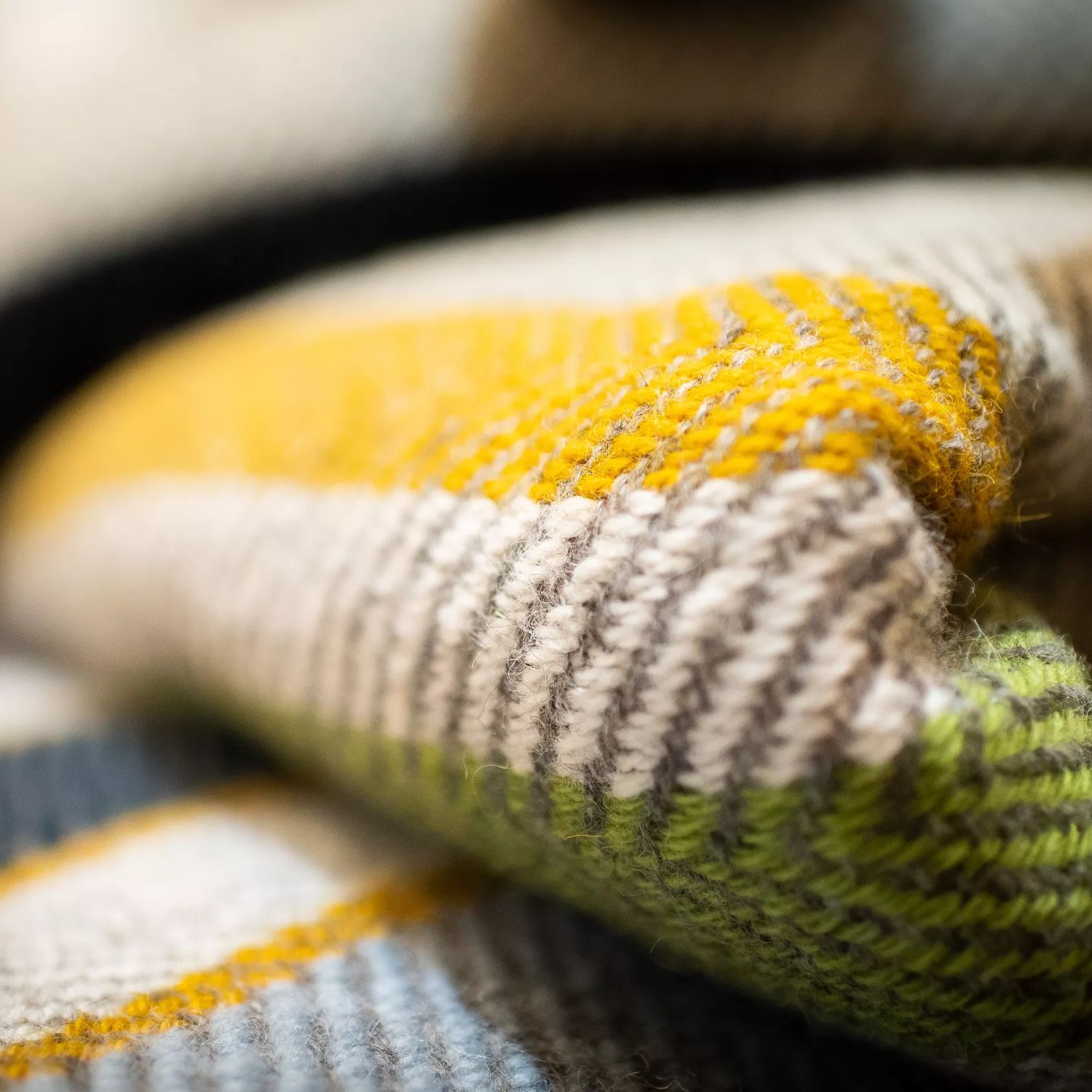 A close-up of a folded knit blanket. The blanket is light grey with yellow, green and navy blue stripes.
