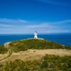 The trail around Pencarrow Lakes and Eastbourne Lighthouse. Green hills meet with the blue ocean and lakes, and the white lighthouse is in the distance.