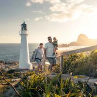 A family walks up steps away from the Castlepoint lighthouse with plants surrounding and sun shining behind them.