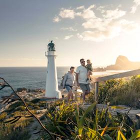 A family walks up steps away from the Castlepoint lighthouse with plants surrounding and sun shining behind them.