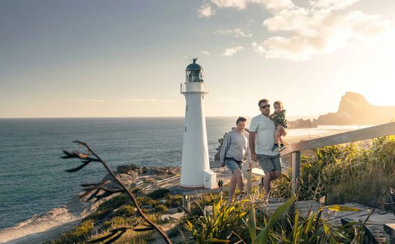 A family walks up steps away from the Castlepoint lighthouse with plants surrounding and sun shining behind them.