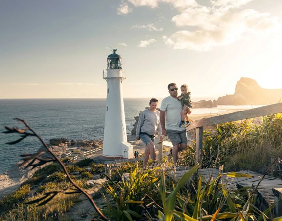 A family walks up steps away from the Castlepoint lighthouse with plants surrounding and sun shining behind them.