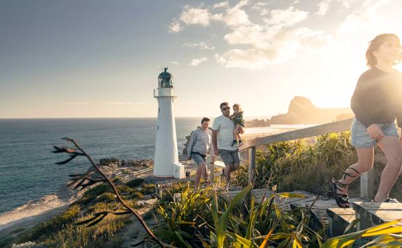 A family walks up steps away from the Castlepoint lighthouse with plants surrounding and sun shining behind them.