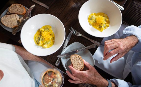 Looking down on hands holding a piece of toast and 2 pasta dishes.