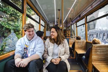 Two smiling people sit beside each other while riding the Cable Car in  Wellington.