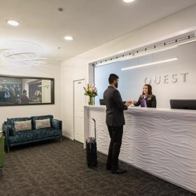 A person is checking in at the front desk at Quest Atrium, a 4 star hotel located on The Terrace in Wellington Central.