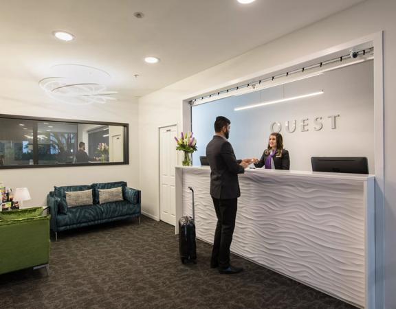 A person is checking in at the front desk at Quest Atrium, a 4 star hotel located on The Terrace in Wellington Central.