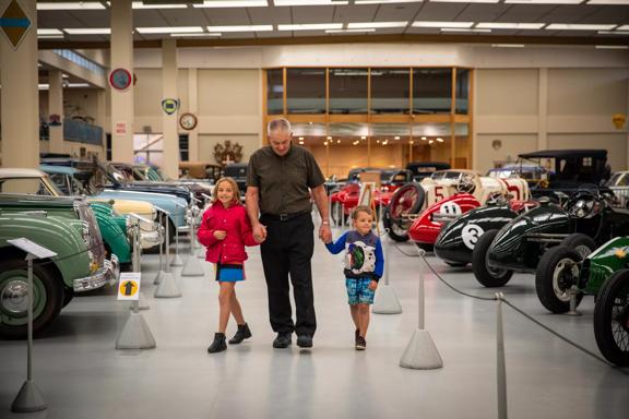 A grandpa and grandchildren walking through vintage  cars at the Southward Car Museum.