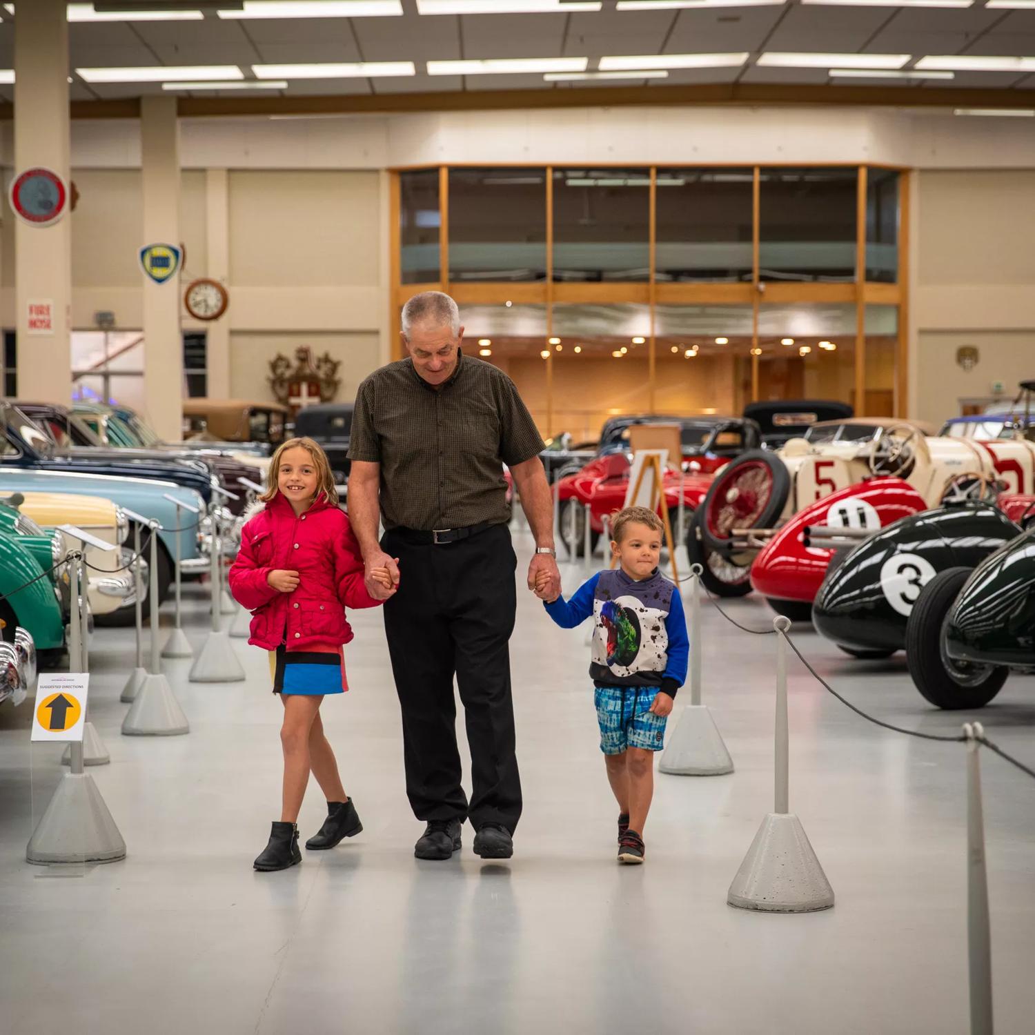 A grandpa and grandchildren walking through vintage  cars at the Southward Car Museum.