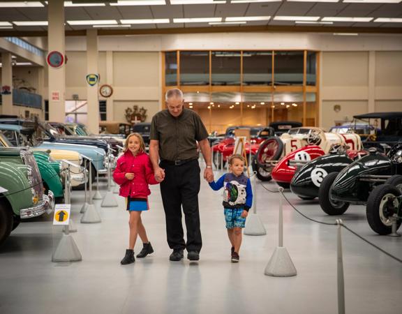 A grandpa and grandchildren walking through vintage  cars at the Southward Car Museum.