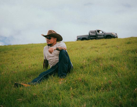 Maoli wearing a cowboy hat sitting on a grassy hill.