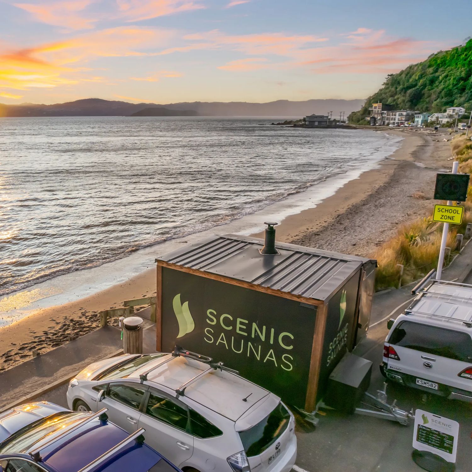 A Scenic Sauna cabin sauna parked on the beach in Days Bay, Eastbourne. The sun is setting over the hill.