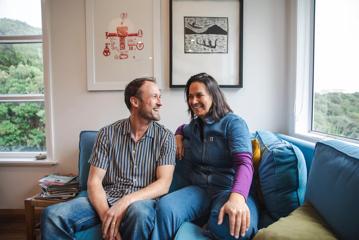 Producers of 'Bloke of the Apocolypse',  Francesca Carney and Ben Powdrellsit, smile and sit on a blue couch together.