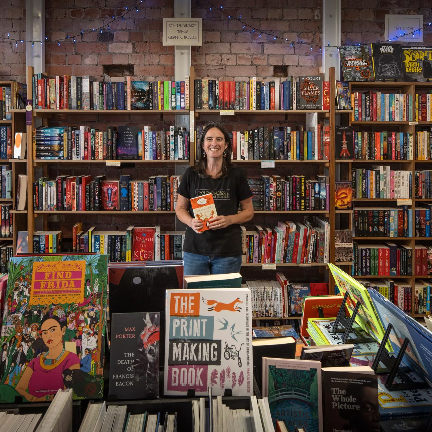 A smiling shop owner stands amongst shelves filled with books at Schrödinger's Books store in Petone.