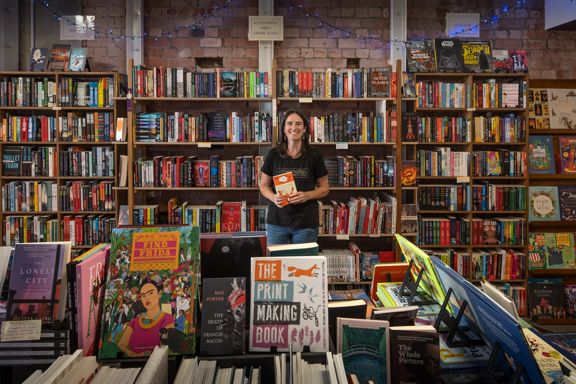 A smiling shop owner stands amongst shelves filled with books at Schrödinger's Books store in Petone.