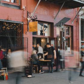 The exterior of a busy wine bar and restaurant with patrons filling both interior and exterior seating.