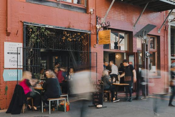 The exterior of a busy wine bar and restaurant with patrons filling both interior and exterior seating.