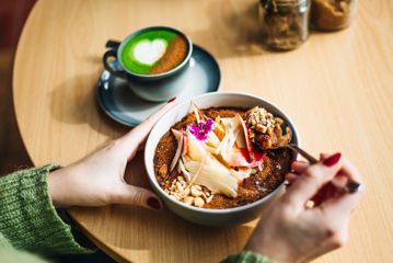 A close-up of a bowl from The Oatery, with colourful toppings on it. There is a green matcha with a heart on it next to the bowl.