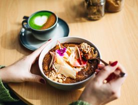 A close-up of a bowl from The Oatery, with colourful toppings on it. There is a green matcha with a heart on it next to the bowl.
