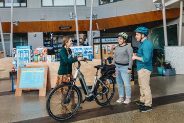 A worker explains e-bike controls to two cyclists.