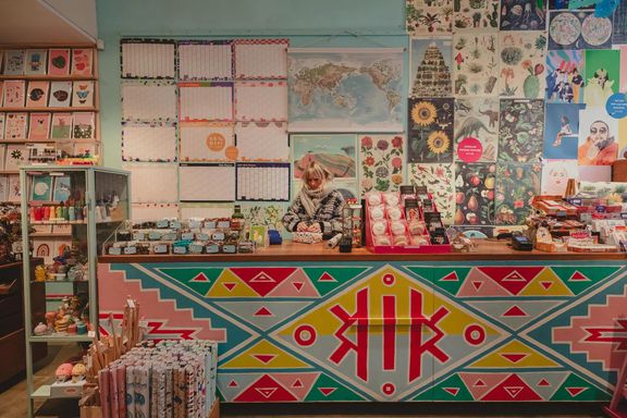 The vibrant interior of Iko Iko with a staff member wrapping presents. Celndars and posters adorn the walls and the counter is painted with red, blue and yellow triangles.