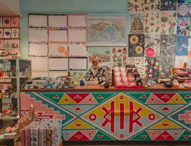 The vibrant interior of Iko Iko with a staff member wrapping presents. Celndars and posters adorn the walls and the counter is painted with red, blue and yellow triangles.