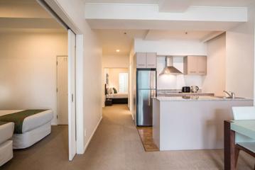 Inside a hotel suite with beige walls a small kitchen and two bedrooms.