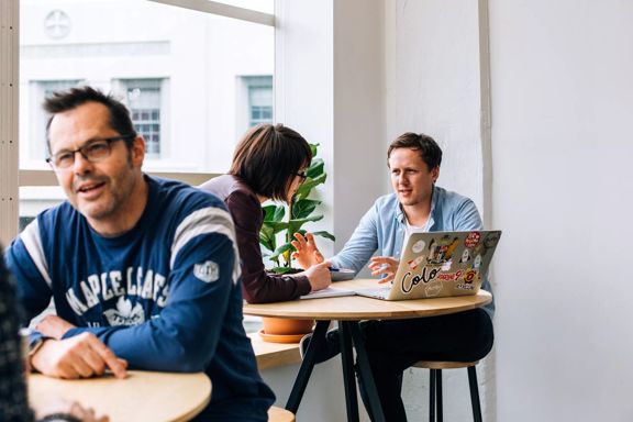 Looking over at two colleagues working at a small high table at BizDojo, Wellington.