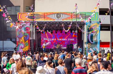 The Ngā Taniwha stage at CubaDupa 2023, with vibrant psychedelic designs surrounding and a large crowd gathered in front.